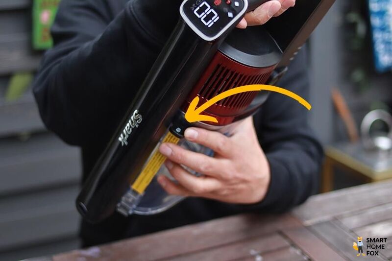 Man sieht den Knopf, um den Schmutzbehälter des Shark Anti Hair Wrap Flexology abzunehmen.